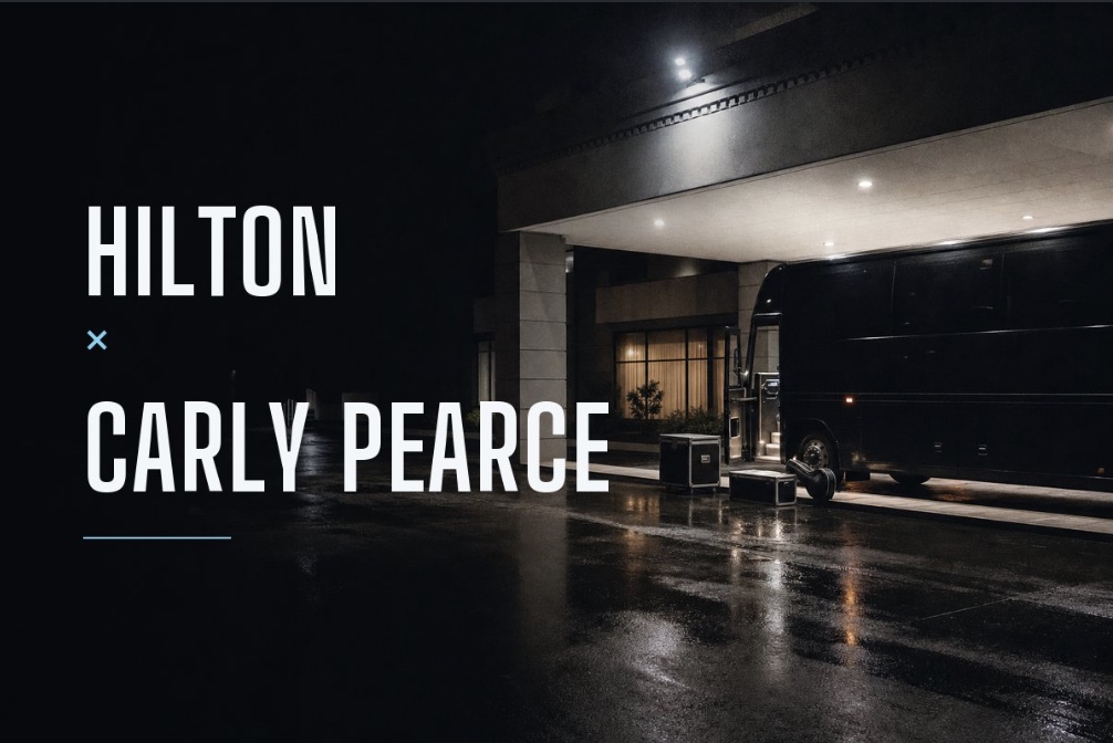 Illustrative concept card for Hilton and Carly Pearce. A tour bus pulled up at a hotel entrance on a wet night.